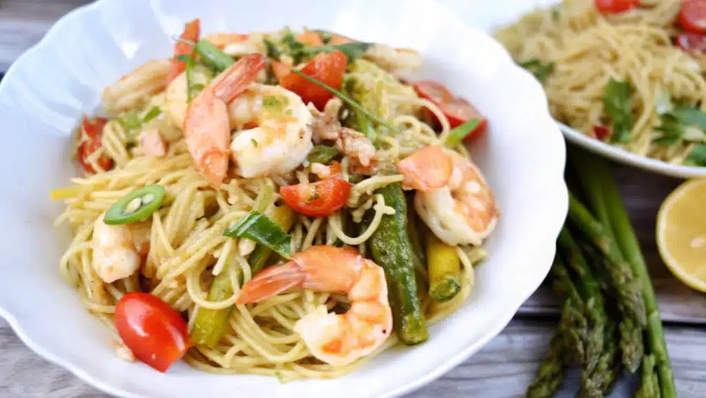 A close-up of Olive Garden Shrimp Scampi showcasing creamy garlic sauce, perfectly sautéed shrimp, and pasta, garnished with parsley and lemon slices, with a glass of white wine and breadsticks in the background."






