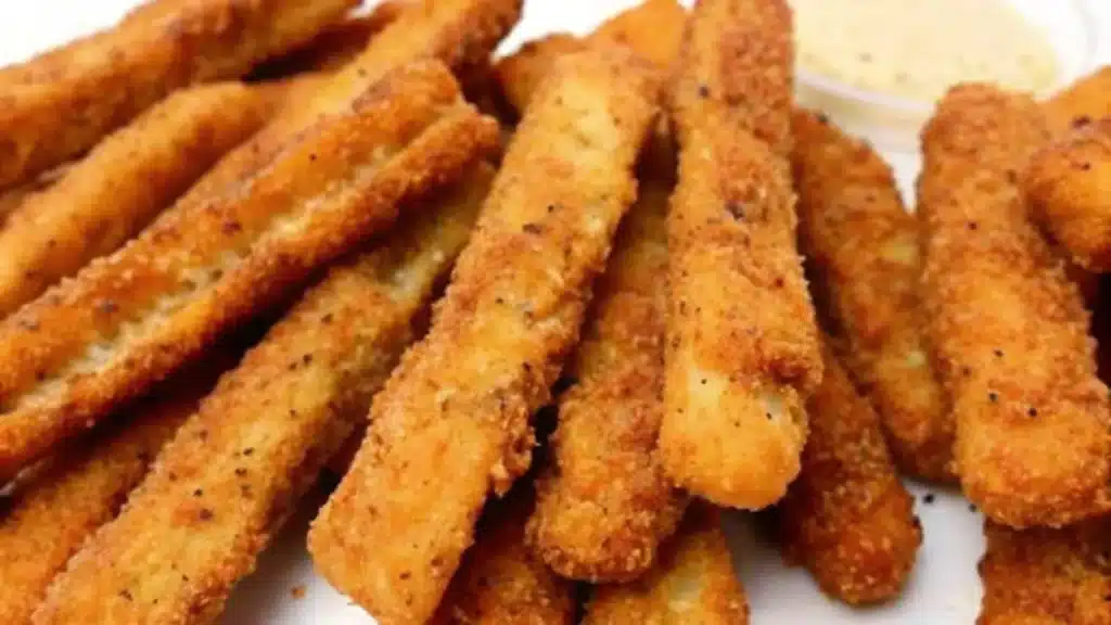 Crispy golden-brown chicken fries cooked in an air fryer, stacked neatly on a plate with a dipping sauce on the side.